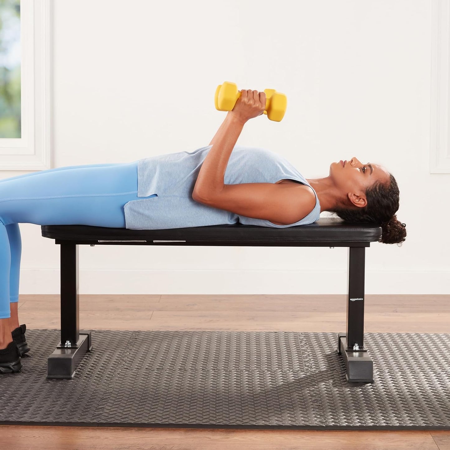 Woman exercising with a yellow dumbbell on a black weight bench indoors.